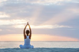 person doing seated yoga at sunrise on beach